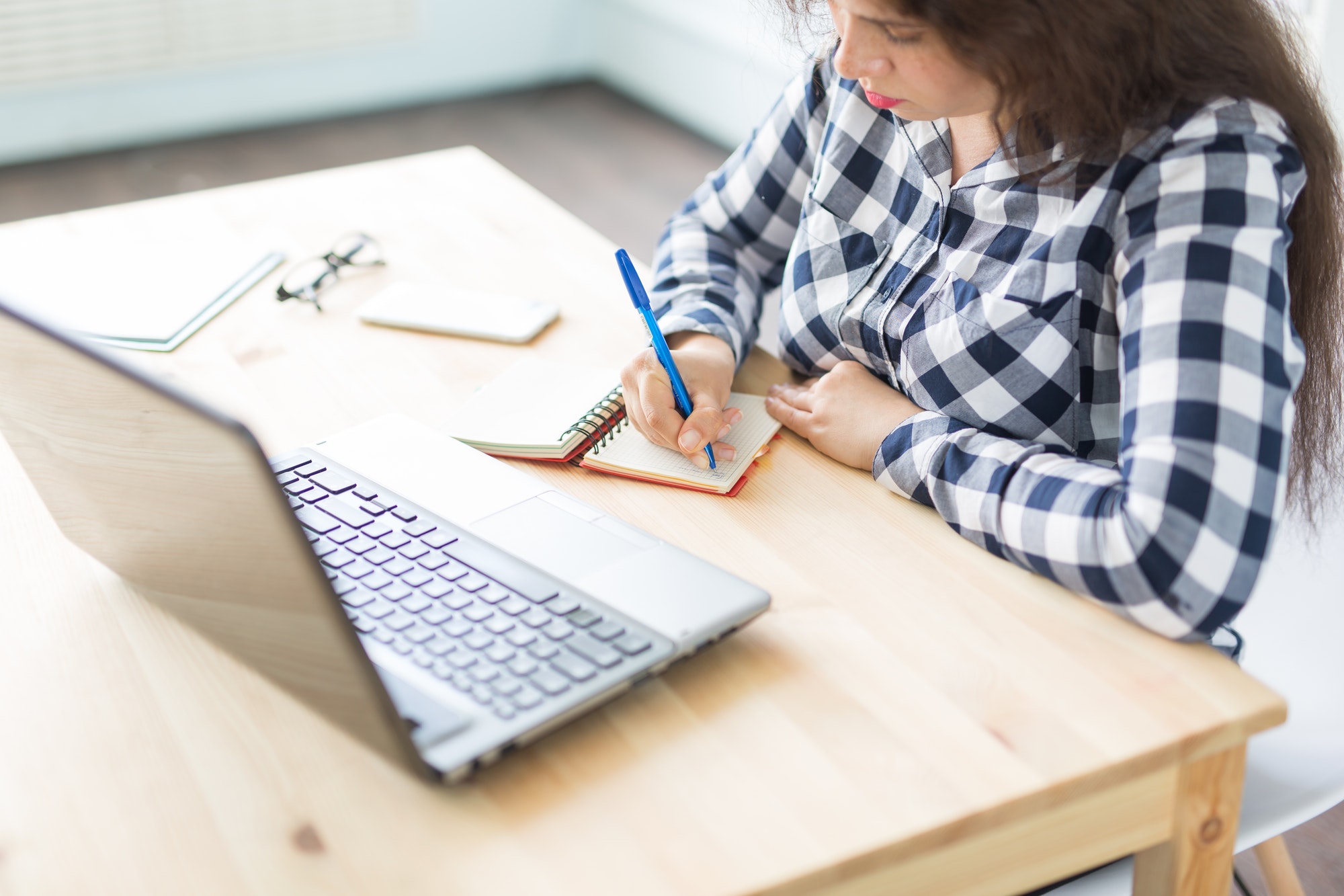 Technology, business and people concept - Close up of woman sitting at her desk and making notes in